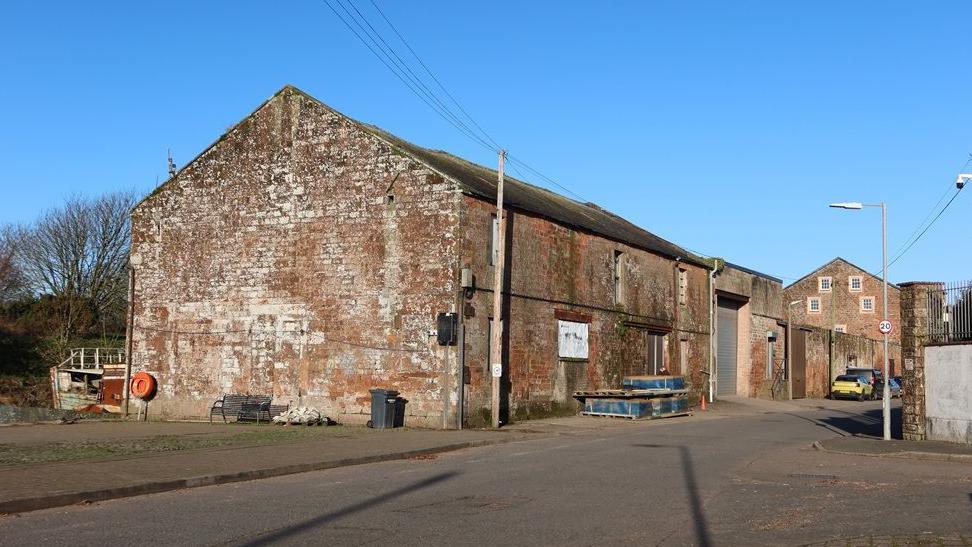 An old brown stone building, next to a road