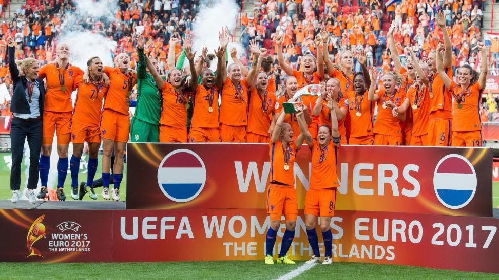 Tîm Yr Iseldiroedd yn dathlu buddugoliaeth Euro 2017 mewn rhes ar gae, gyda dwy chwaraewr yn dal y tlws
