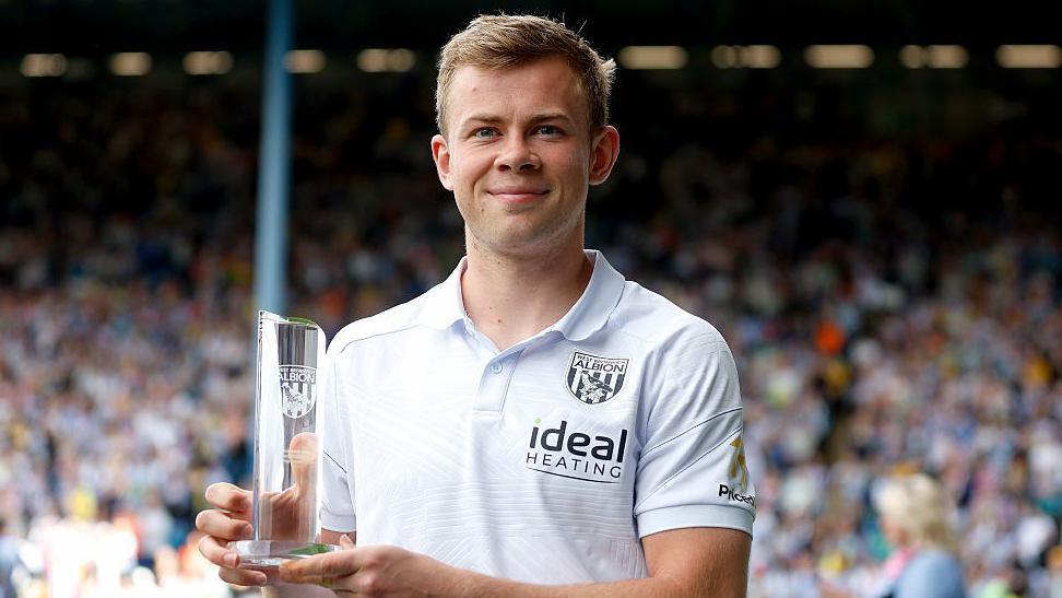 Aune Heggebo is wearing a light grey West Bromwich Albion polo shirt and is holding the club's top scorer trophy for his 10 goals across all competitions for the club last season.