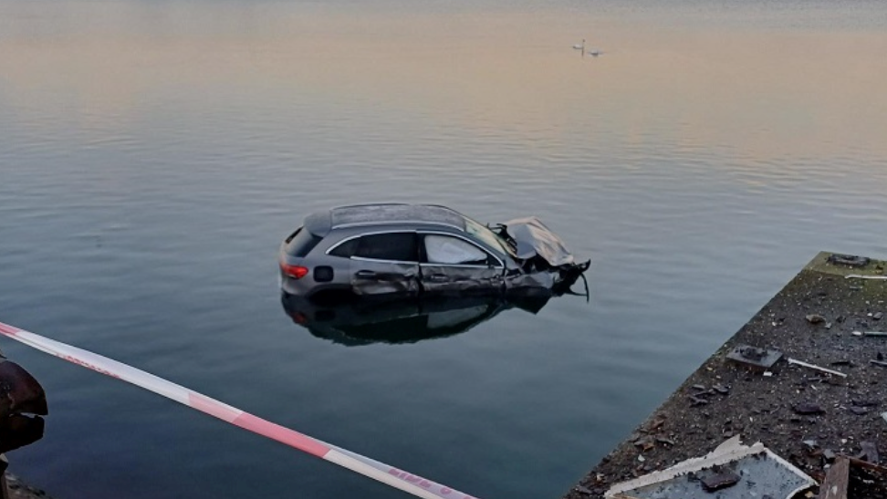 A silver Mercedes car with severe damage to its bonnet and driver's side, partially submerged in shallow water.