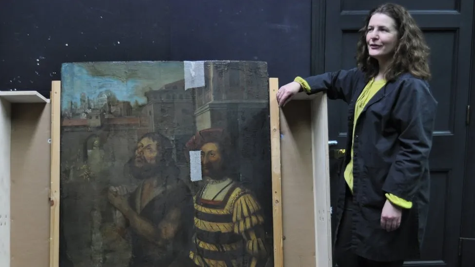 Brown-haired woman standing next to painting depicting the beheading of John the Baptist.