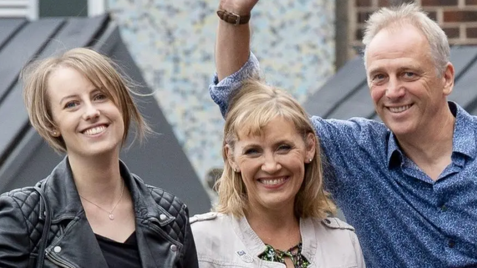 Laura Nuttall smiles as she stands next to her parents. She is wearing a black leather jacket and a black top and she has blonde hair in a bob.