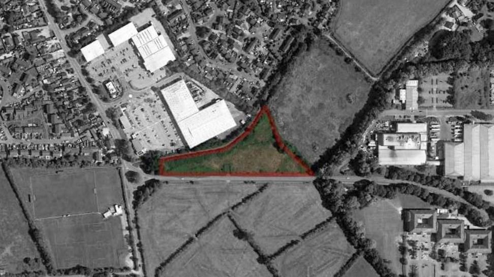 An aerial view of the agricultural land in Trowbridge. There is a green elongated triangular patch in the middle, outlined with red, indicating where the development could be built. The rest of the image has been masked in black and white.