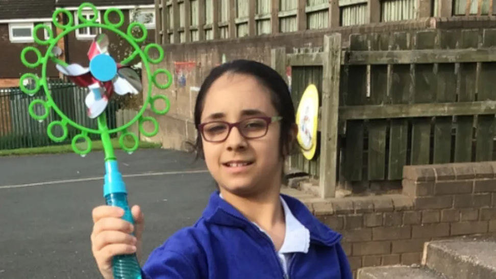 A girl in a blue school uniform jacket waves a bubble blower