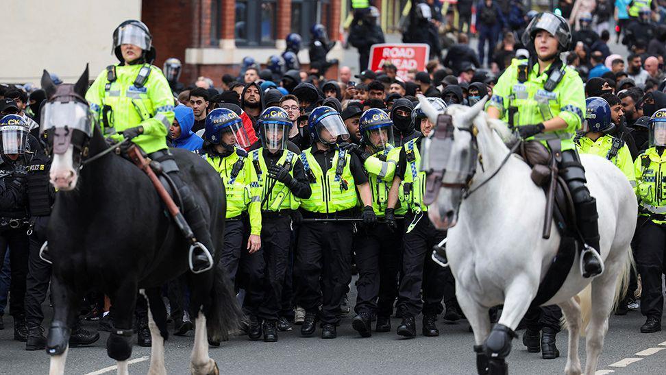 Two mounted police officers line up in front of riot gear-wearing colleagues  in Bolton on 4 August.