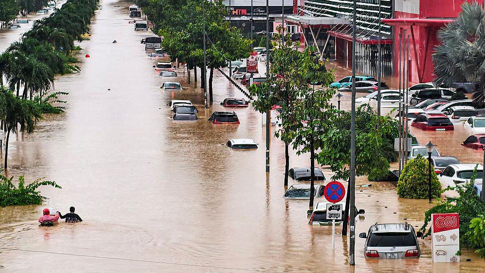 Vehicles inundated while two people hold on to each other as they wade through floodwaters in the city of Nha Trang