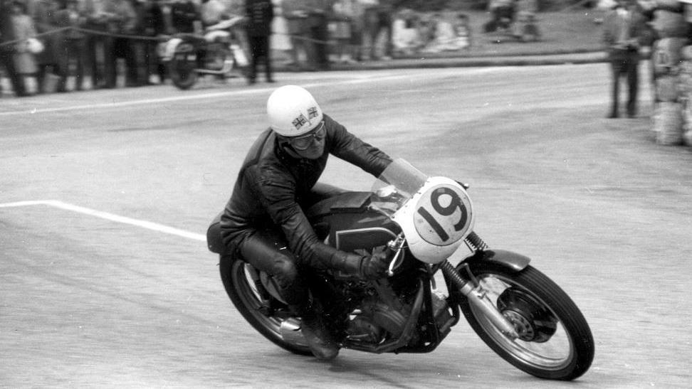 A black and white photograph Ron Langston competing on a bike with the number 19 on the front. He is wearing black leathers and a white helmet.