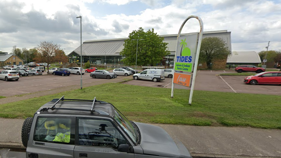 Tides Leisure Centre viewed from Park Road, showing the outside of the building and the car park, with several cars parked there.