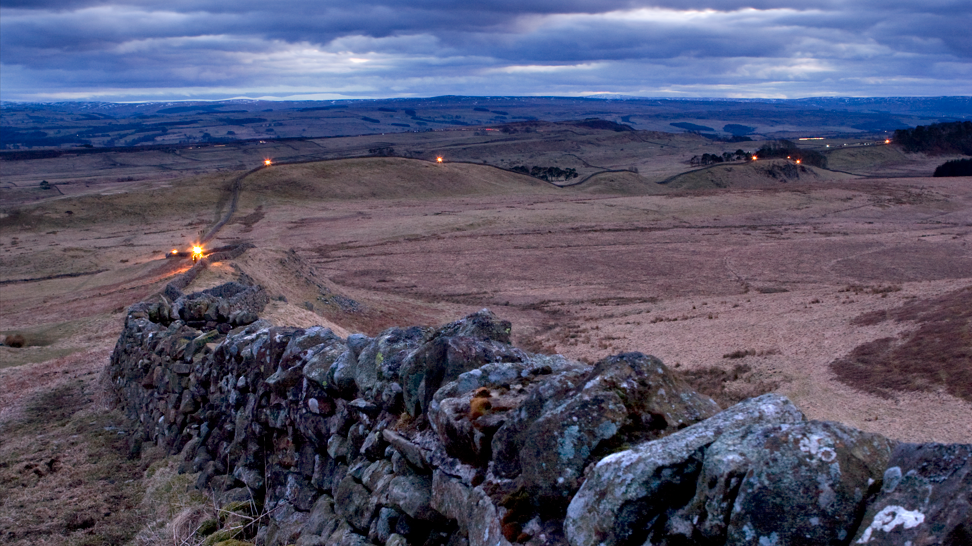 A panoramic view of Hadrian's Wall with beacons lit at points along stretching several miles 