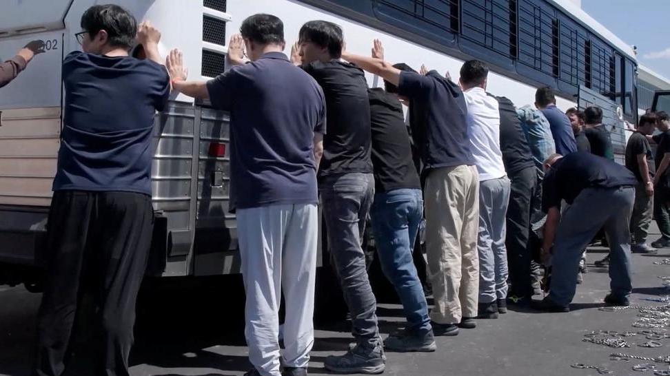A row of detainees are made to stand against a bus before being handcuffed, during a raid by federal agents in Georgia in September
