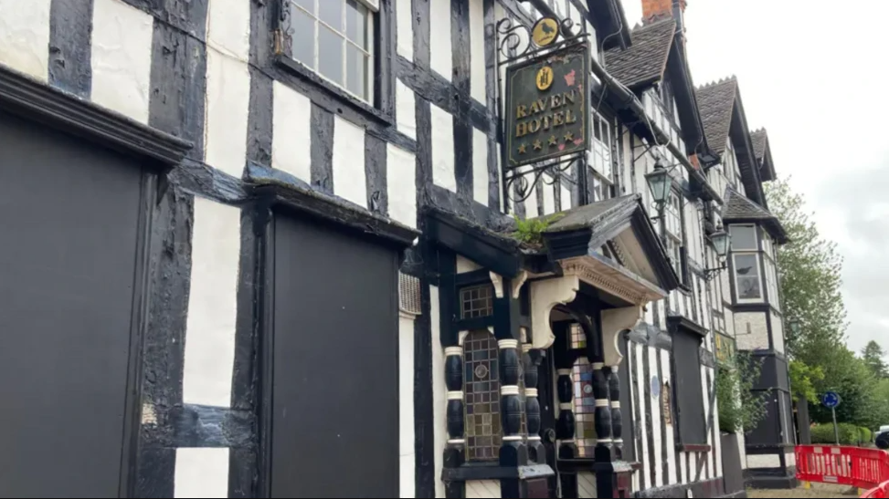 Exterior photo of a black and white timber building with a sign hanging outside reading "Raven Hotel".