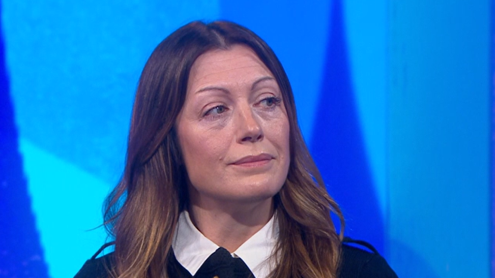 Mel Popham is in the Newsnight studio. She has long brown wavy hair and is wearing a dark coloured jacket with brass buttons and a white blouse.