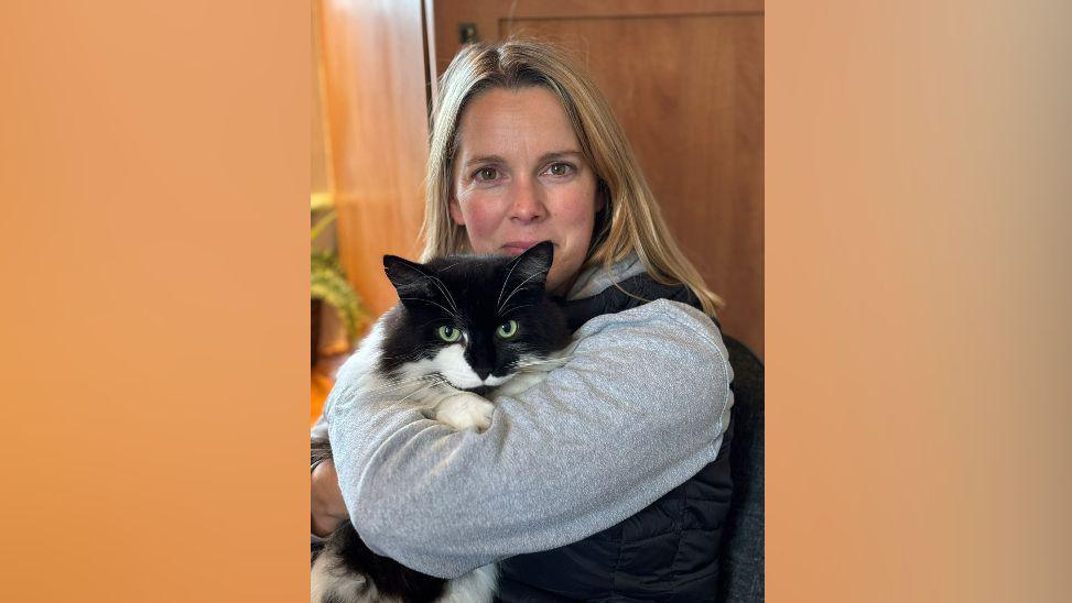 A blonde woman holding a black and white cat.