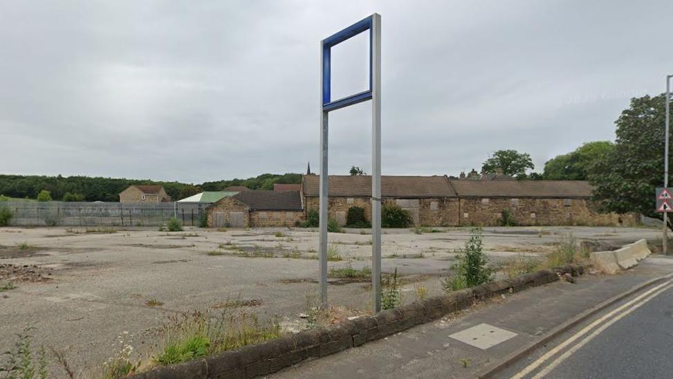 An empty, overgrown concrete area by the side of the road 