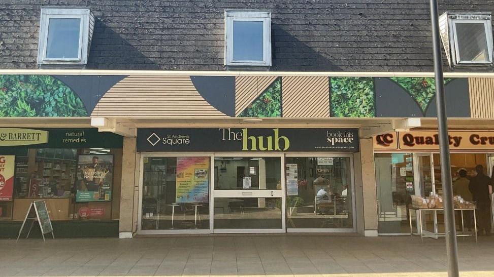 The Hub shop front photographed on a sunny day. The premises' front shows a class entrance with a dark grey sign that reads "The Hub" in white and green writing.
