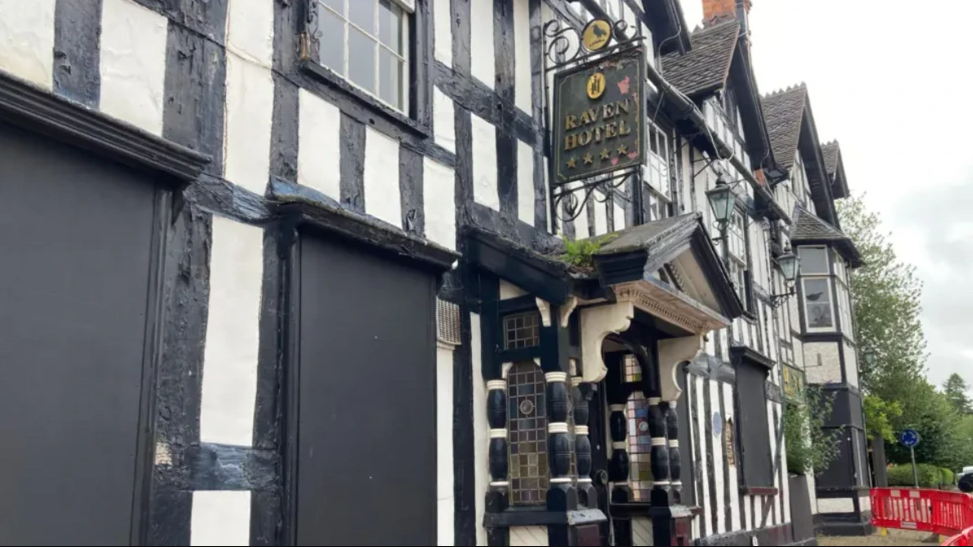 Exterior shot of a black and white timber building with a sign hanging outside reading "Raven Hotel".