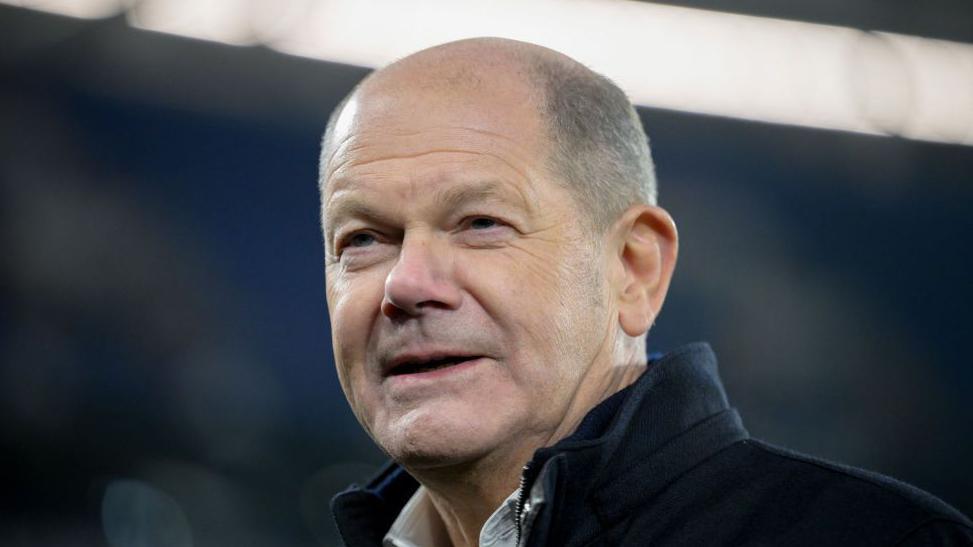 German chancellor Olaf Scholz smiles as he stands in a football ground in Gelsenkirchen