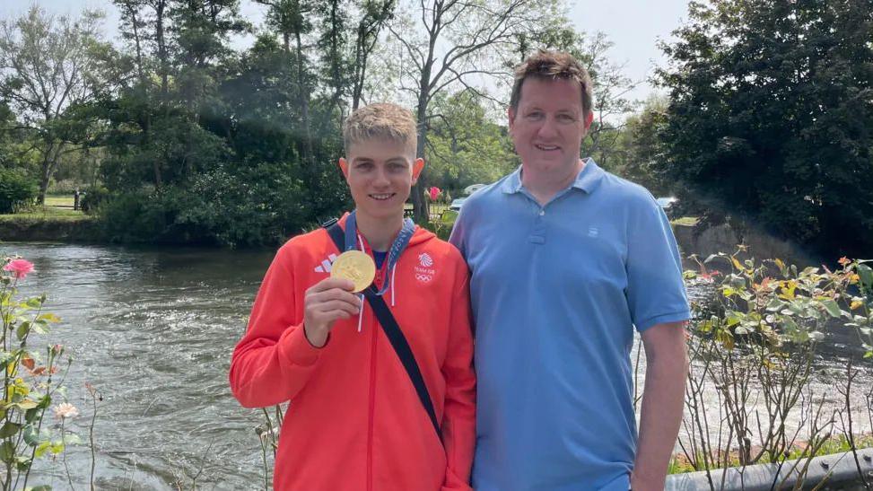 Toby Roberts holding his gold medal next a man in a blue shirt