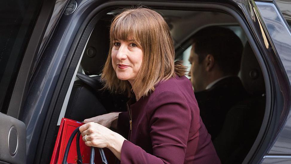Chancellor Rachel Reeves getting out of a cab outside Downing Street in May, wearing a maroon suit and carrying a handbag and red folder