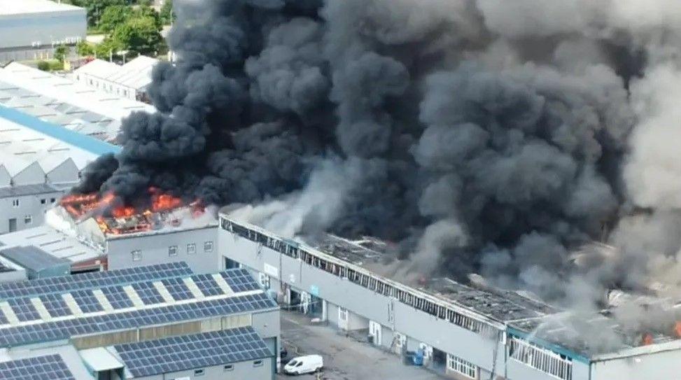 An industrial unit in flames, with plumes of black smoke rising into the air