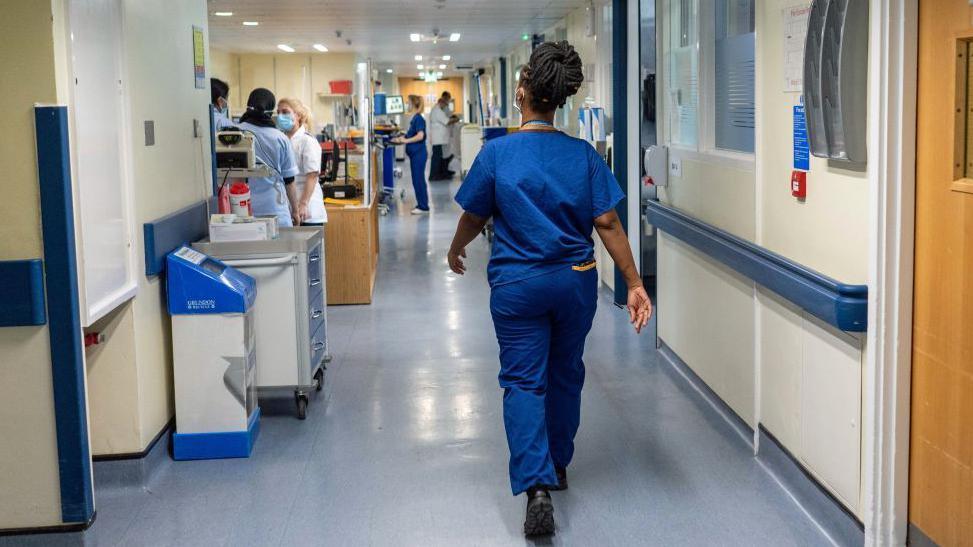 Nurse from behind walking down a busy hospital corridor