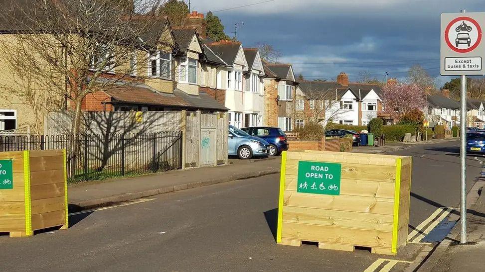 Two wooden road blocks with signs on saying the road is open to pedestrians, scooters, wheelchairs and cyclists