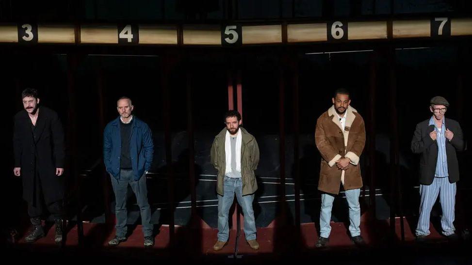 Five man lined up on stage under dole queue numbers for the stage production of Boys From The Blackstuff at Liverpool's Royal Court