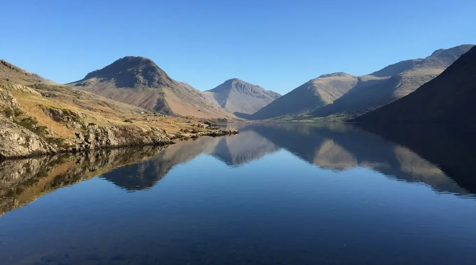 A scenic lake in the Lake District is surrounded by mountains.