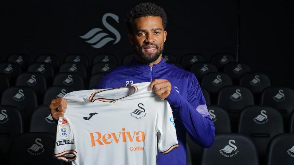 Cyrus Christie holding up Swansea shirt