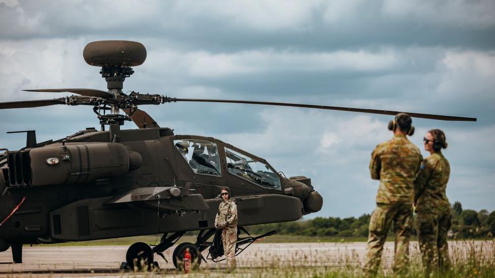 Soldiers in the foreground with an Apache helicopter in the background