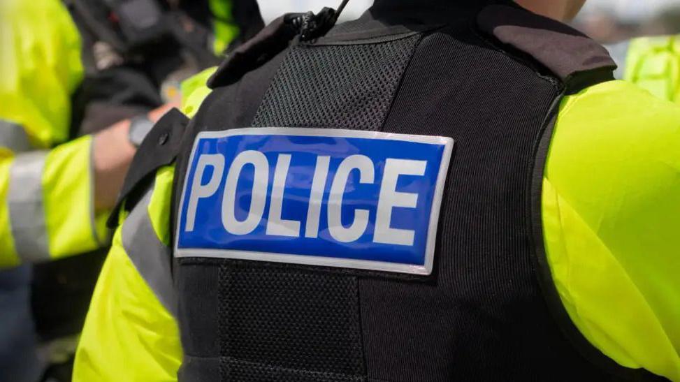The back of a person wearing a black police vest with the word POLICE written in white on a blue background