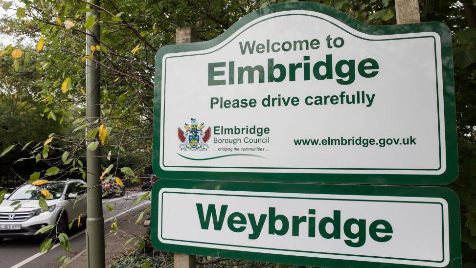 A sign for Elmbridge on the side of a road.