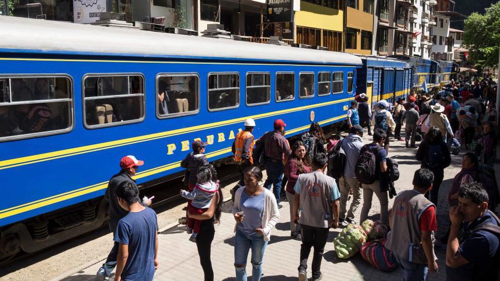 A train at the station in Aguas Calientes, with people standing on the platform