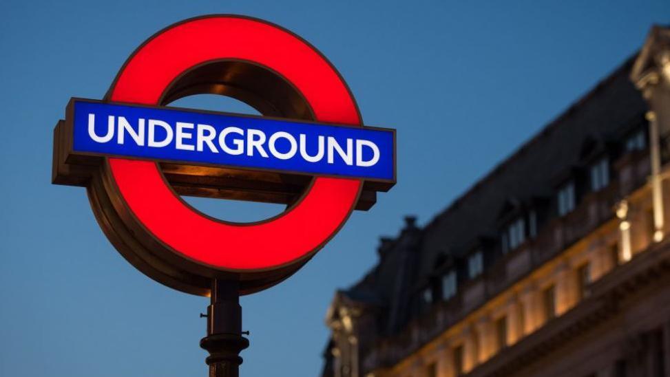A lit-up London Underground sign on a dark street