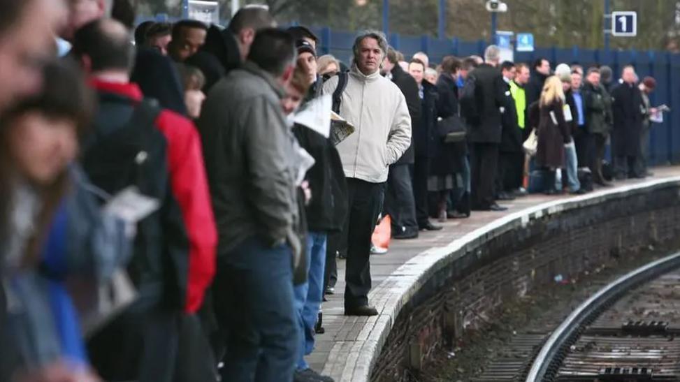 A crowd of passengers on a platform await a train.