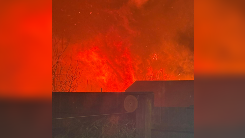 Orange flames appearing behind a wooden fence and a house. 