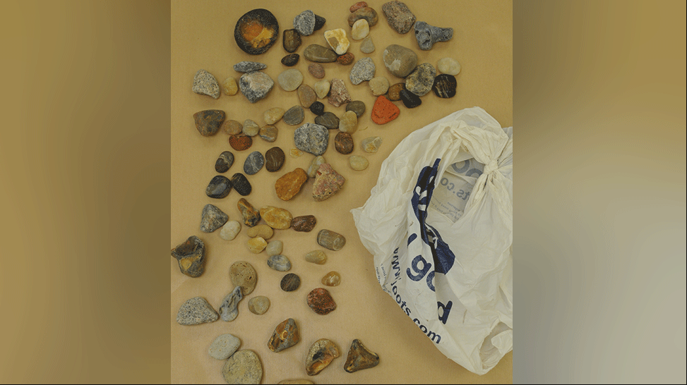 Decorative stones and pebbles laid out on a table next to a white Boots carrier bag