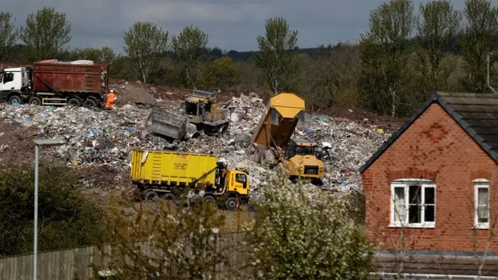 Vehicles moving rubbish at Walleys Quarry, as piles of rubbish are seen at the site, near a house and lots of trees