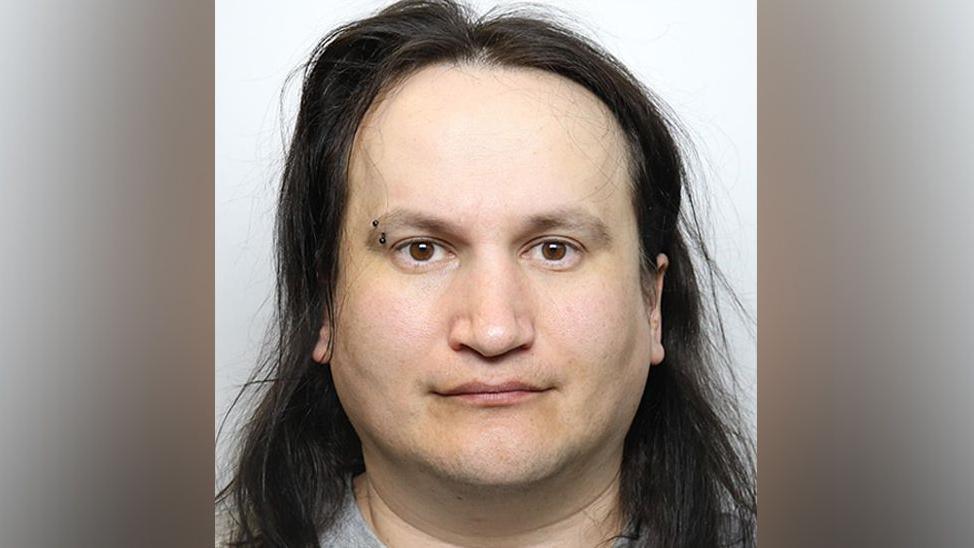 Custody image of Marcin Majerkiewicz with a brow piercing, long dark brown hair and wearing a grey t-shirt.