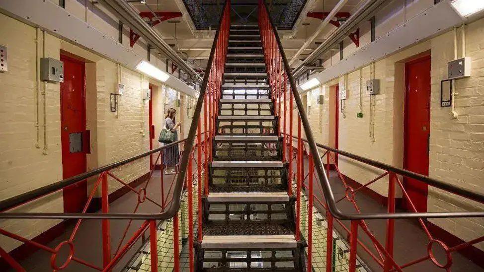 Stairwell with red bannisters and open hallways with cream walls and red doors either side.