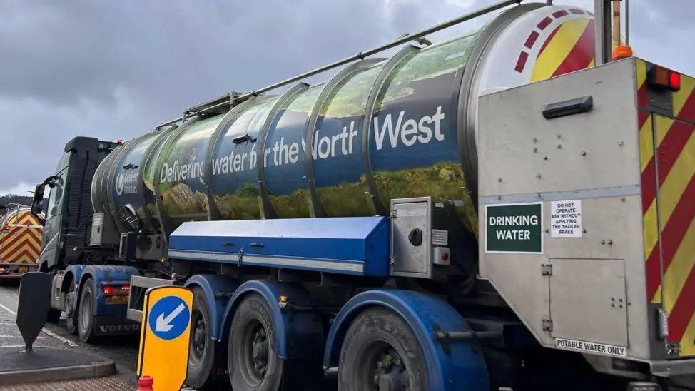 A water tanker with the words 'delivering for the North West' sits in traffic on an overcast day. 