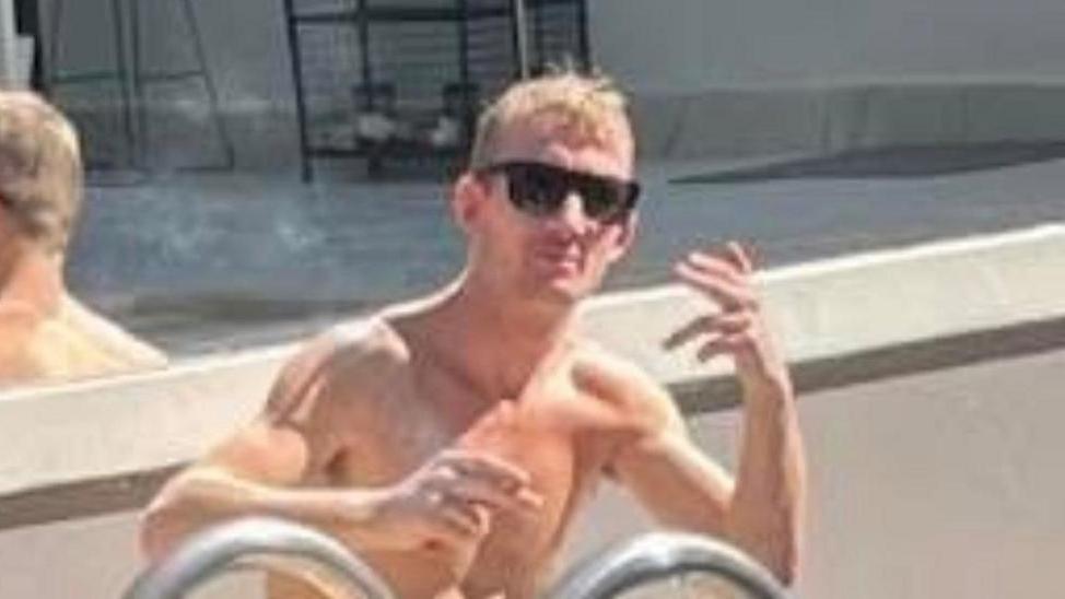 Craig Yorke. He is sitting next to a pool with his shirt off and wearing sun glasses.