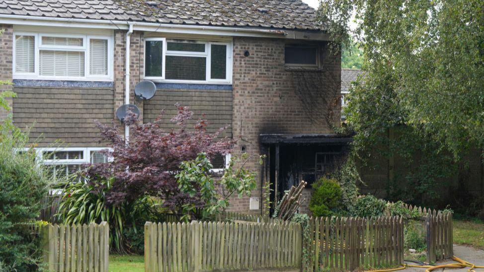 A residential home is scorched after an arson attack. There is some green plants in front of the house.