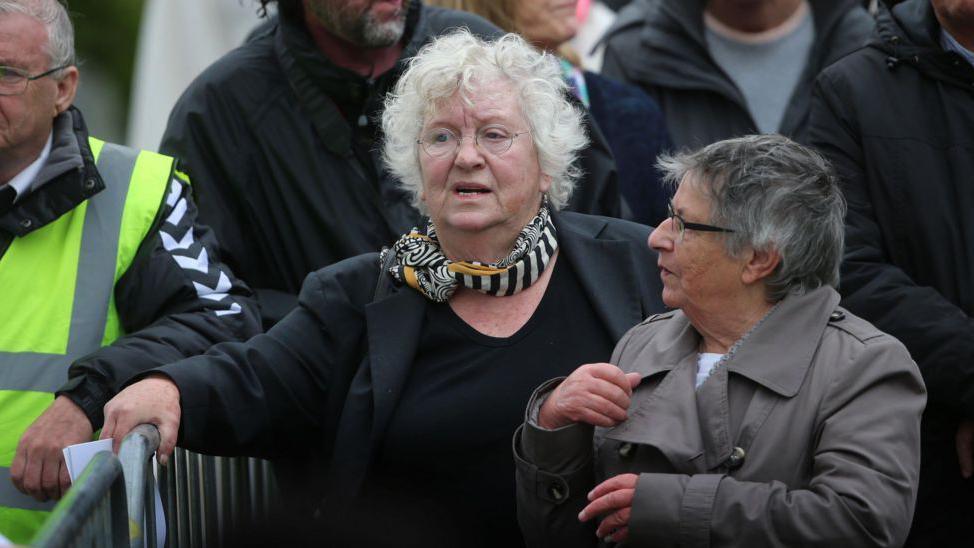 Nell McCafferty walking and talking with with another woman, her hand on a metal barrier
