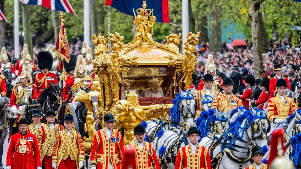 The King and Queen can be faintly seen within a golden carriage flanked by horses and servicemen and women.