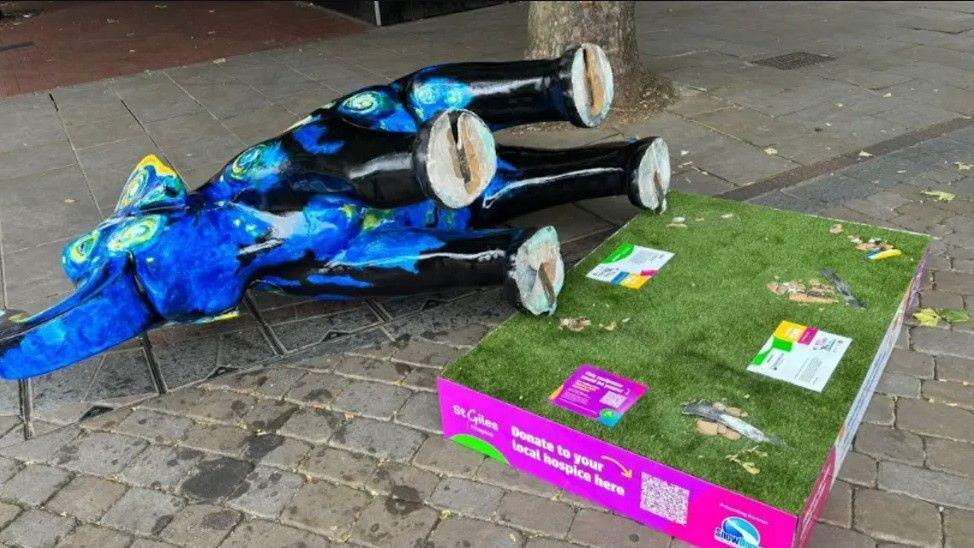 A blue Vincent Van Gogh Starry Night themed elephant lies on its side on the ground, next to the green fake grass topped plinth it was originally on