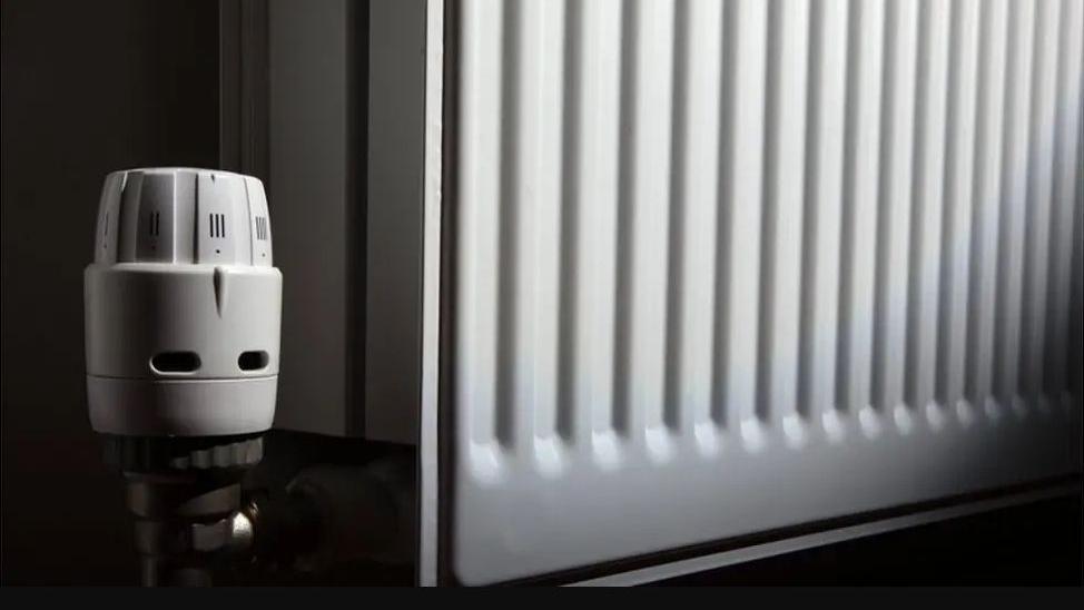 A white metal radiator, with the control knob the focus in the foreground.