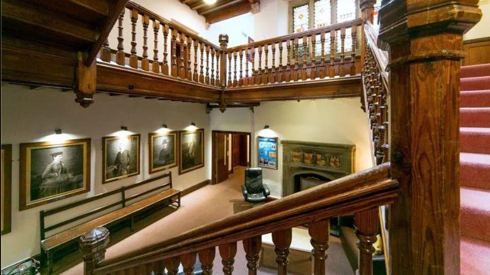 View of a carved wooden staircase curving round the photo with portraits hung on the walls below