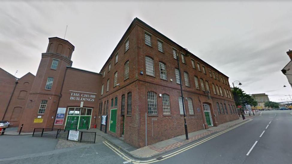 A brick building on a street corner with a sign saying 'The Chubb Buildings'. Its doors are bright green.