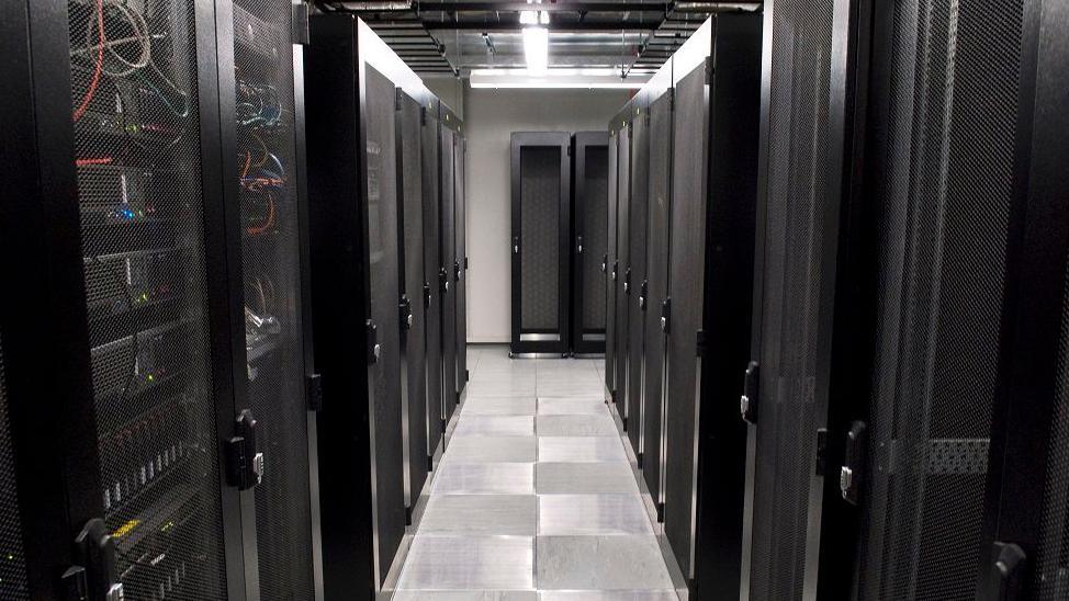 Narrow corridor in data centres with racks of computer servers behind smoked glass on either side